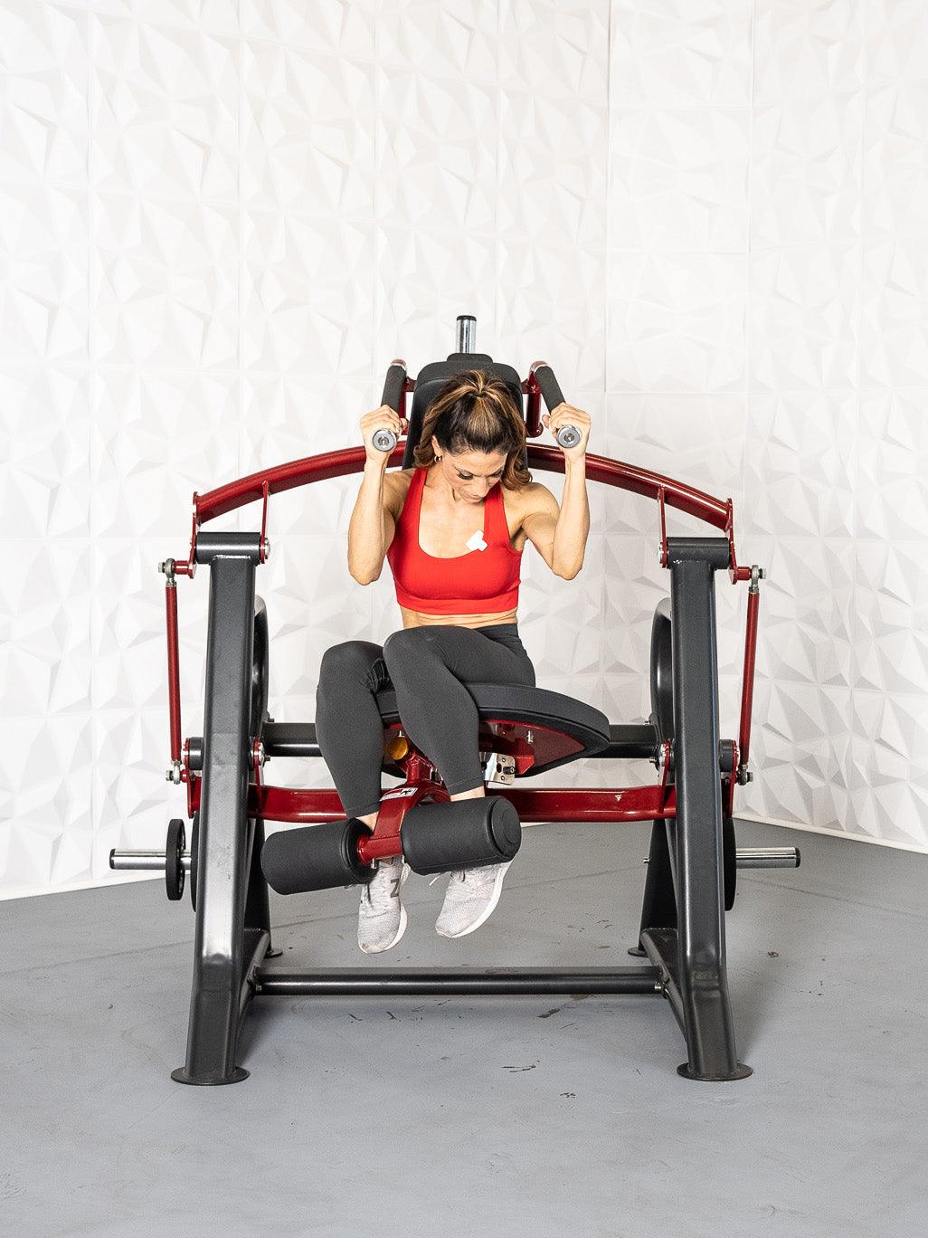 Woman in red sports bra and black leggings using a seated, plate-loaded abdominal crunch machine.