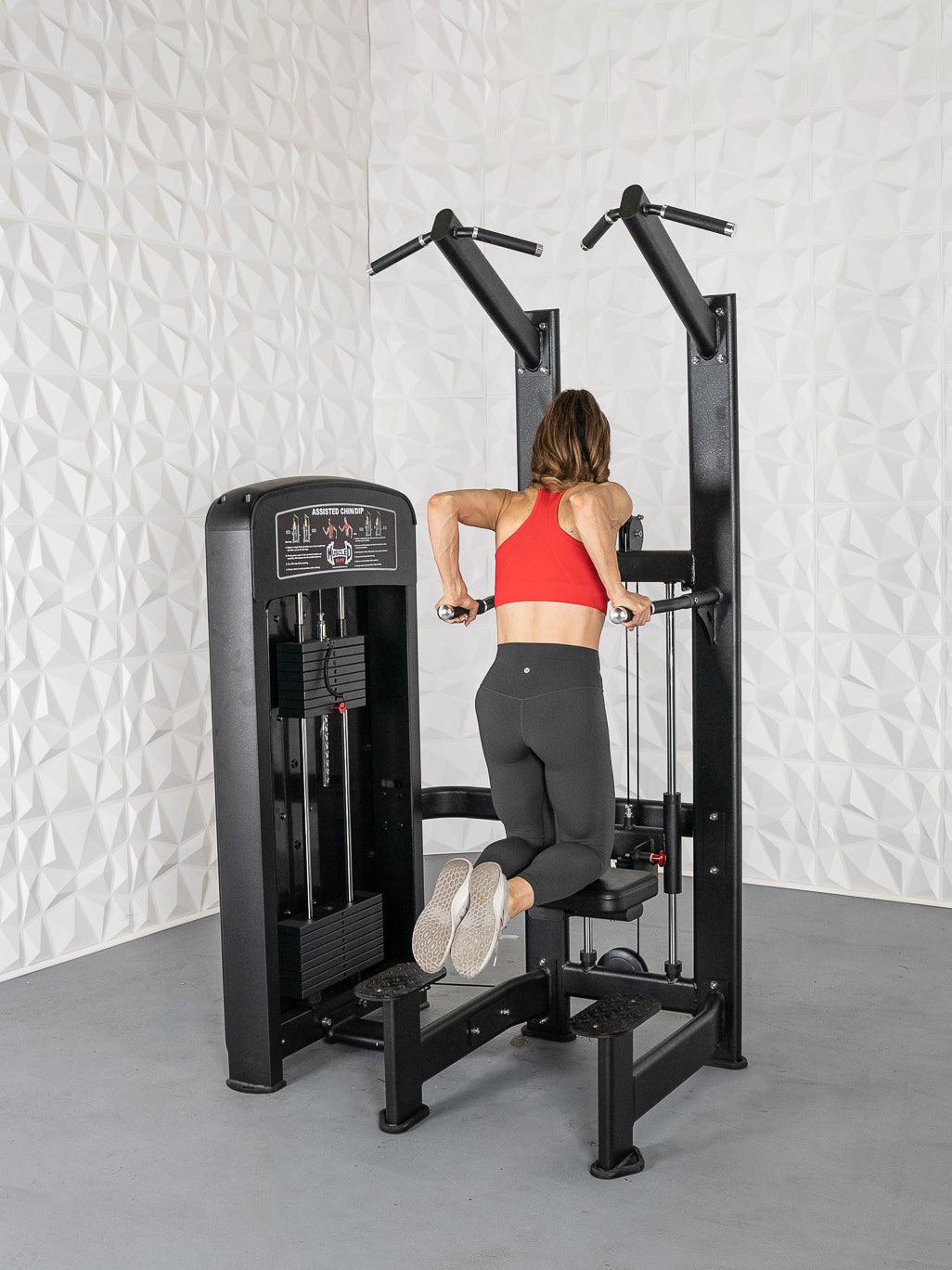 Woman in red top and black leggings using a black assisted chin/dip machine.