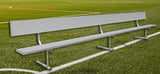 Long silver portable bench with a backrest on a green sports field.