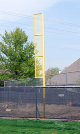 Yellow foul pole with mesh panels, extending above a baseball field fence against a blue sky.