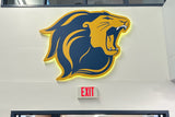 Backlit acrylic sign of a navy and gold roaring lion head on a white wall above an exit sign
