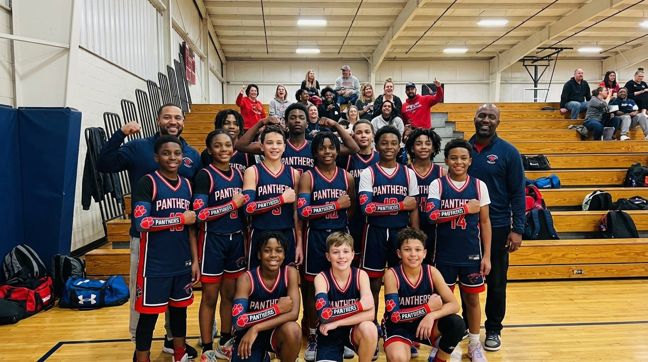 Basketball team wearing blue jerseys and red arm sleeves, posing with coaches on a court.