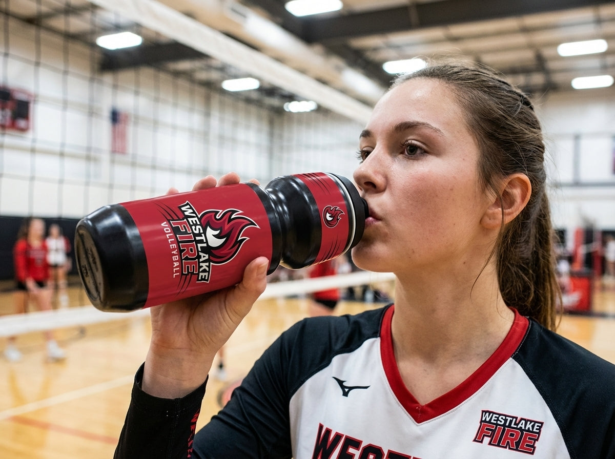 Volleyball player in a white and black jersey drinking from a red water bottle with "WESTLAKE FIRE" logo.
