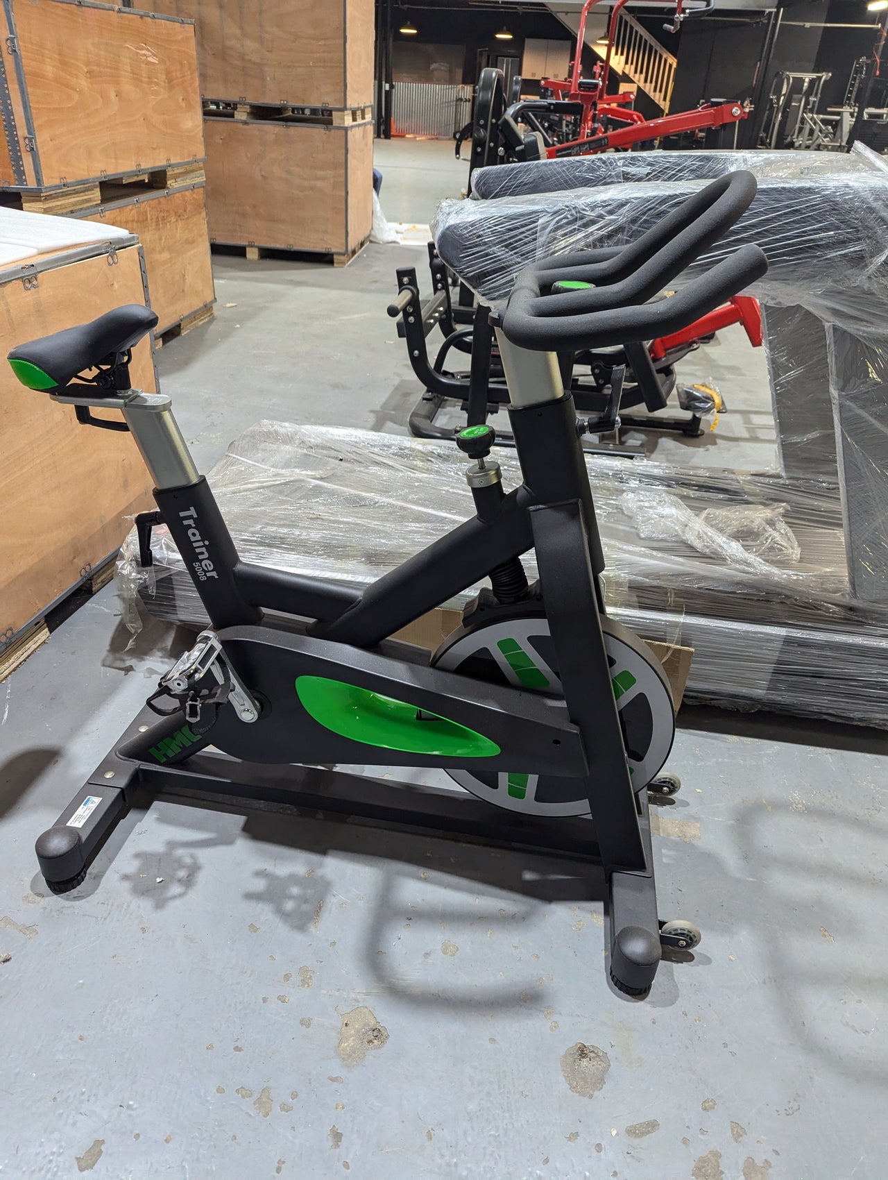 Black stationary exercise bike with green accents in a warehouse setting.