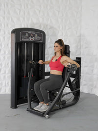 Thumbnail for Woman in red top and gray leggings using a black chest press machine with a weight stack.