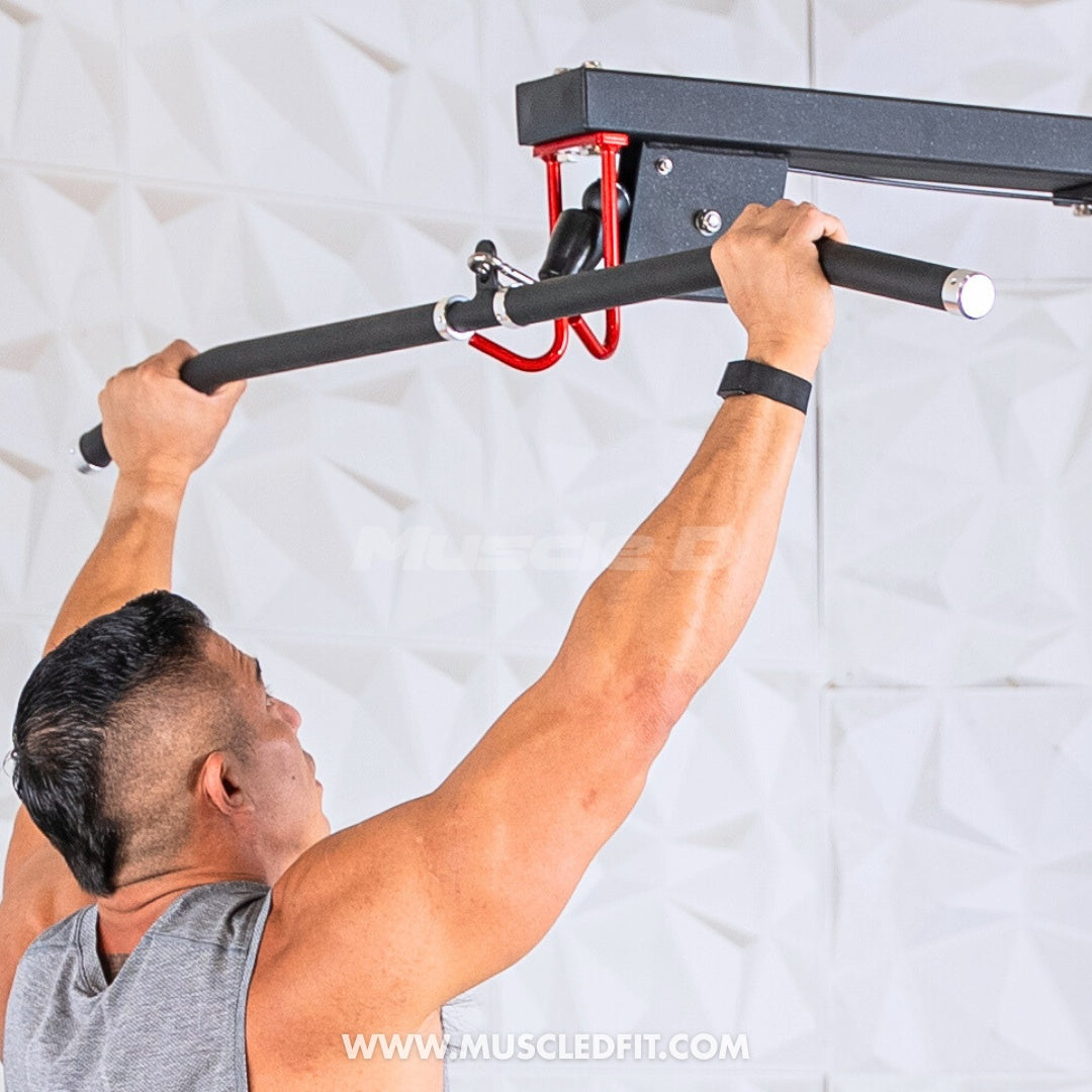 Man in a gray tank top gripping a black lat pulldown bar attached to a wall-mounted gym machine.