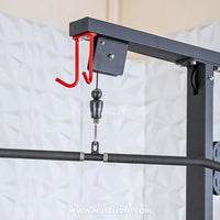 Thumbnail for Close-up of a lat pulldown machine's top pulley system with red accessory hooks and a black bar attachment.