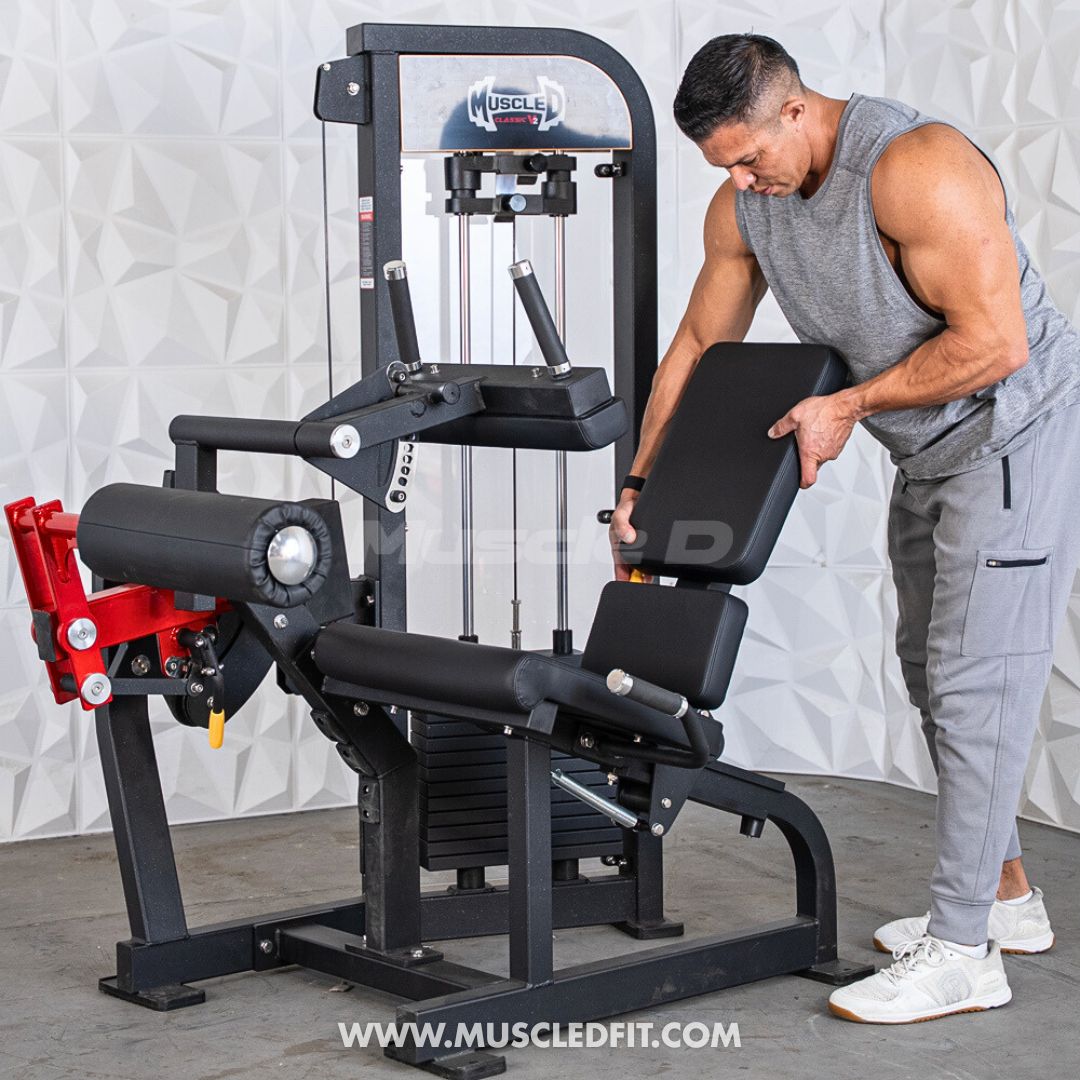 Man adjusting the seat of a black and red leg extension/curl combo machine with a weight stack.
