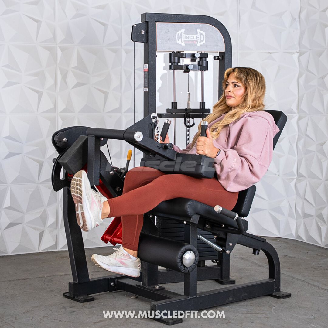 Woman using a black leg extension/curl machine, extending her legs forward.
