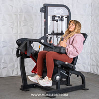 Thumbnail for Woman seated on a black leg extension/curl machine, performing an exercise.