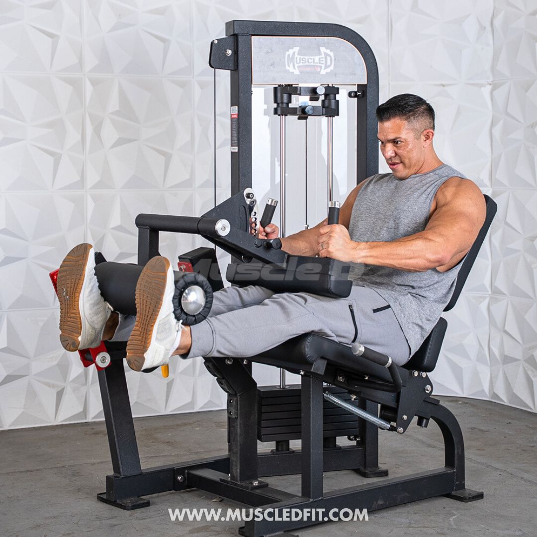 Man performing leg extension on a black selectorized leg extension/curl machine with white textured wall background.