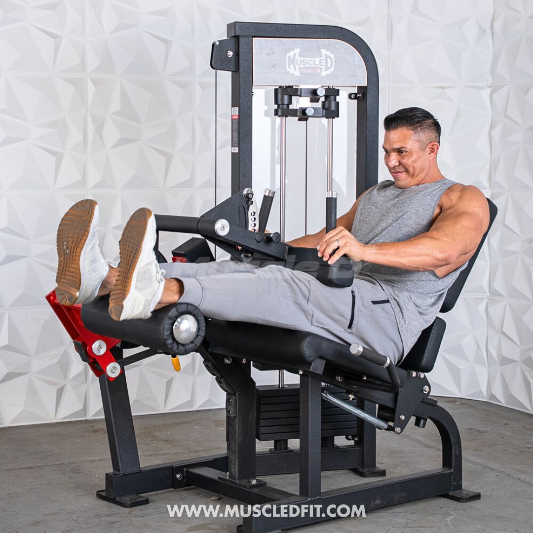 Man using a black selectorized leg extension/curl machine with red accents against a white textured wall.