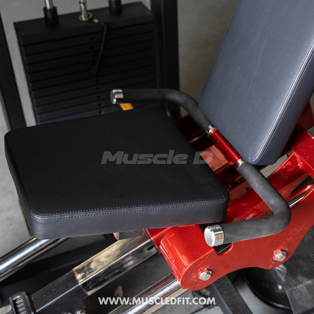 Close-up of a red leg press machine's black seat and backrest, with weight stack visible in the background.