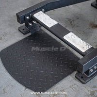 Thumbnail for Close-up of a black standing calf raise machine's foot platform with diamond plate texture and metal foot pads.