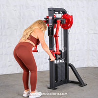Thumbnail for Woman in rust-colored workout gear using a black and red lateral raise machine.