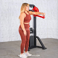 Thumbnail for Woman in rust-colored workout clothes using a black and red lateral raise machine.