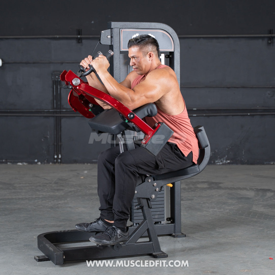 Man using a red and black triceps extension machine in a gym.