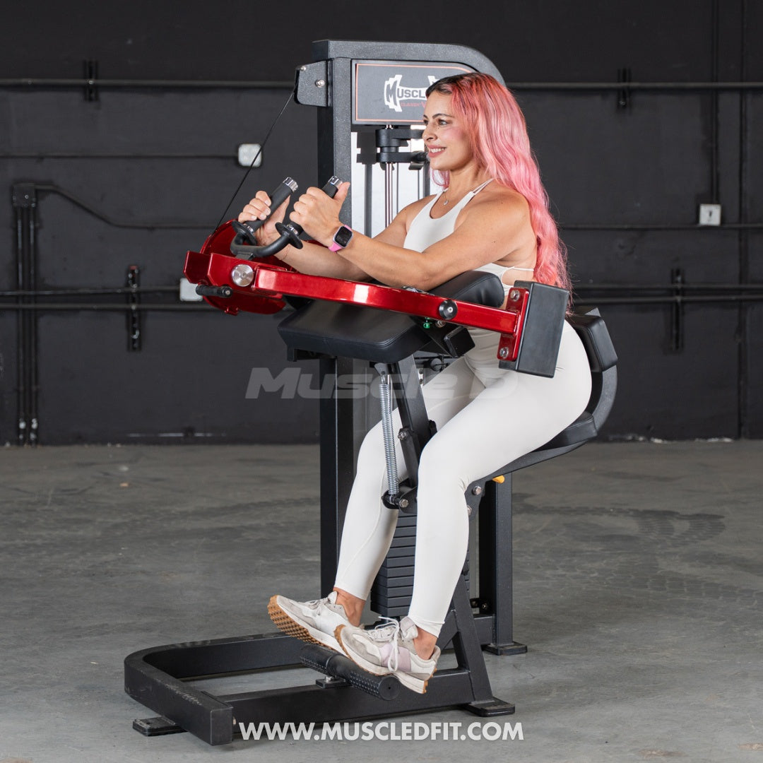 Woman with pink hair using a red and black triceps extension machine in a gym.