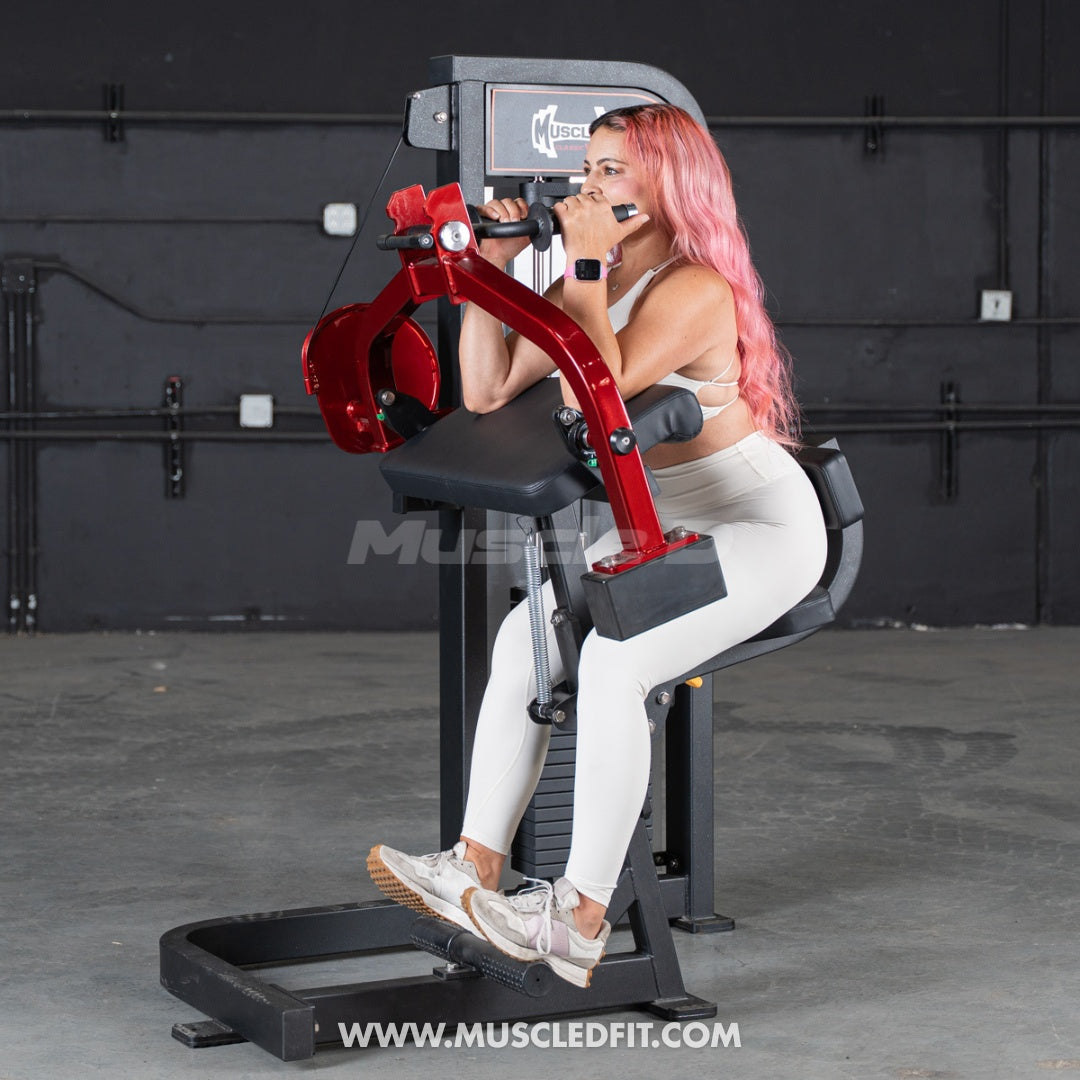 Woman with pink hair using a red and black triceps extension machine in a gym.