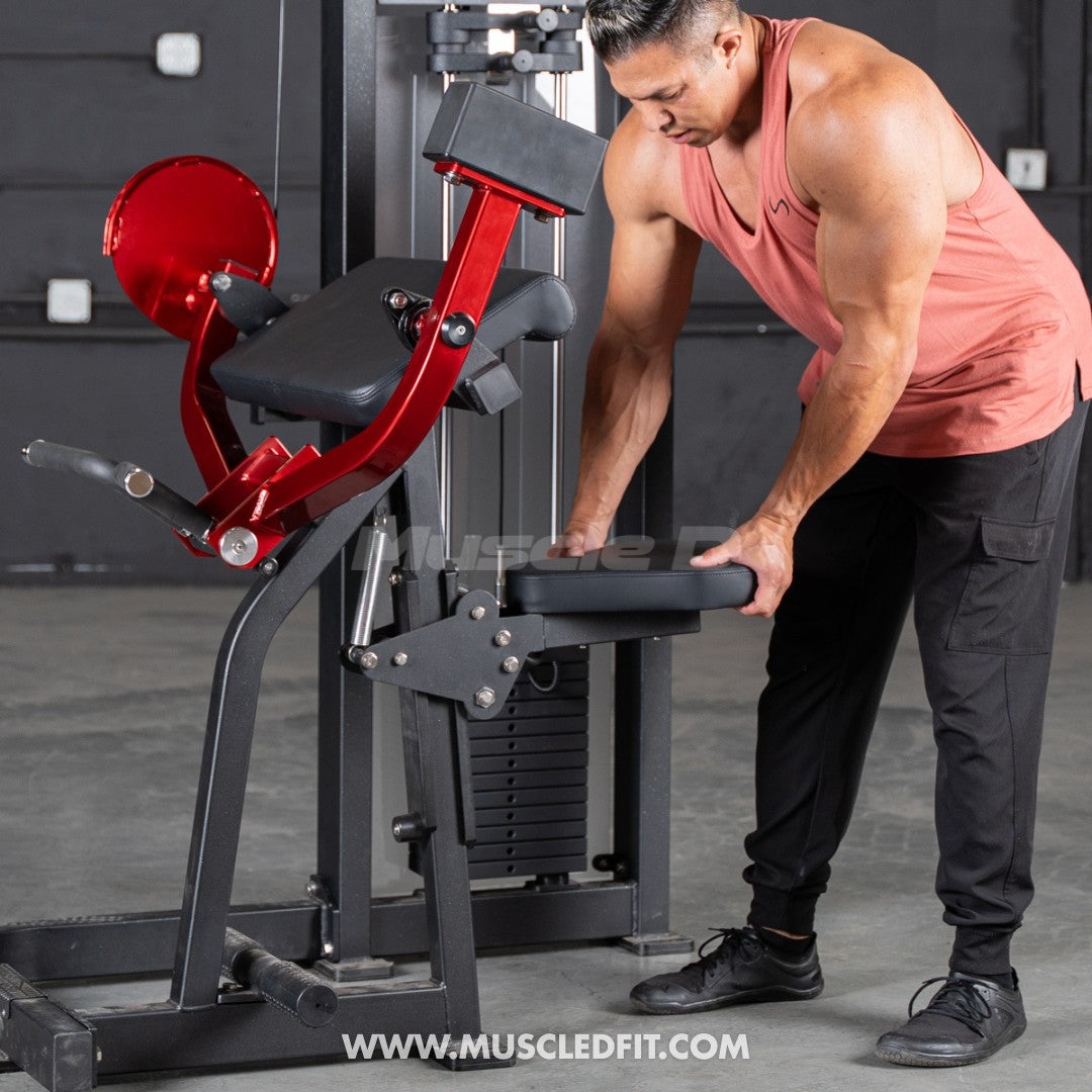 Man adjusting the seat of a red and black biceps curl machine with a weight stack.