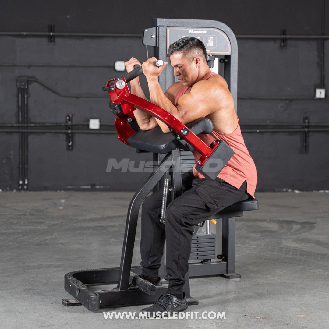 Man in a tank top using a red and black biceps curl machine in a gym.