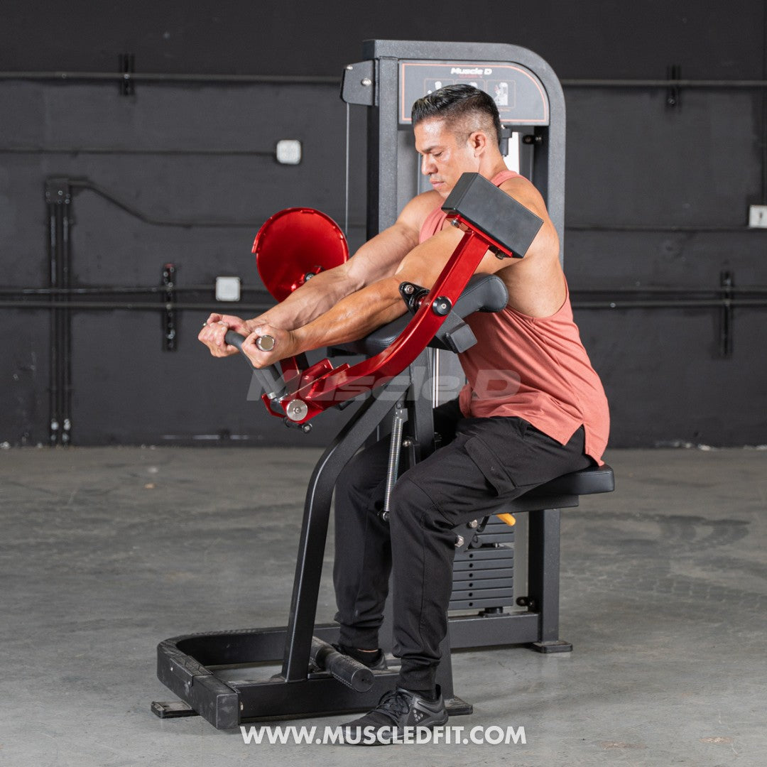 Man in a tank top using a red and black biceps curl machine with a weight stack.