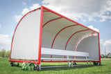 Portable sports team shelter with a white cover, red frame, bench and green sandbags on a grass field