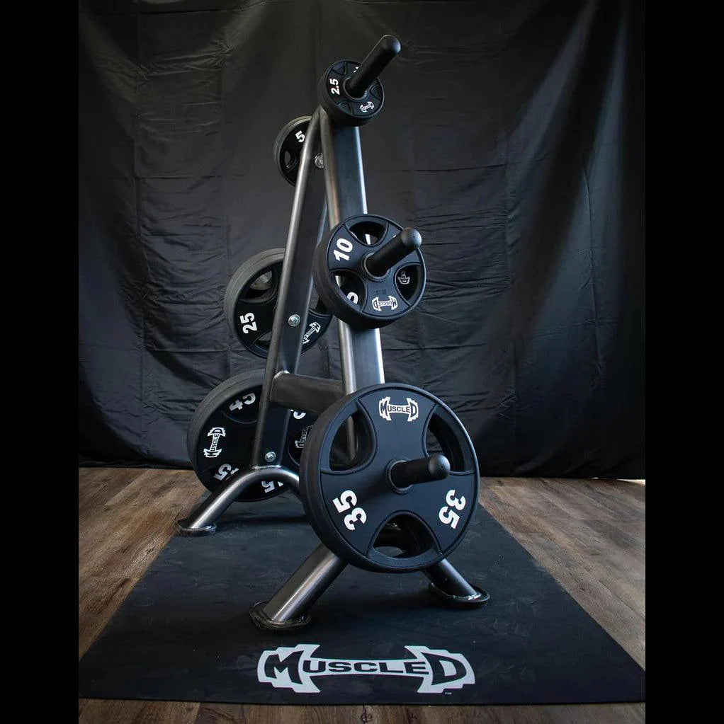 Black urethane-coated Olympic weight plates on a storage rack, with a "Muscle D" mat on a wooden floor.