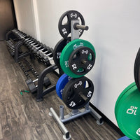 Thumbnail for Green, blue, and black urethane bumper plates on a weight rack with dumbbells in the background.