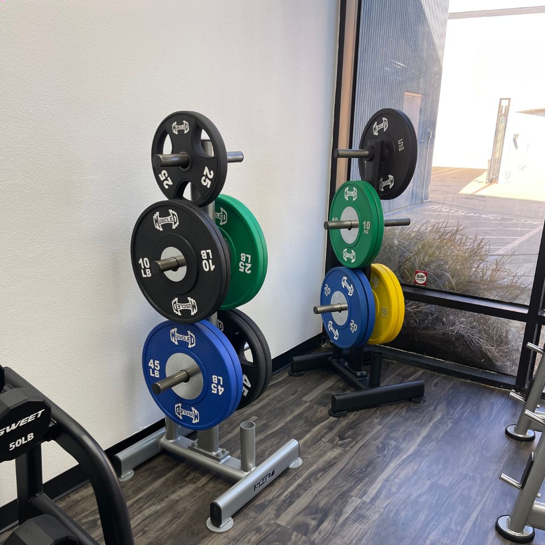 Black, green, blue, and yellow bumper plates on two weight racks in a gym.