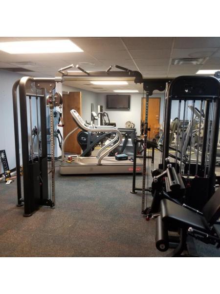 Multi-gym with lat pull, low row, bench press, and leg extension/curl stations in a gym setting.