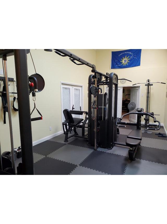 Black 5-stack compact multi-gym with various attachments in a home gym setting with checkered floor.