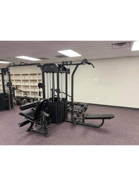 Black multi-gym with various stations, including a lat pulldown and leg curl, on purple carpet.