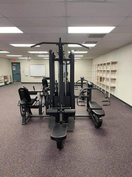 Black multi-gym with multiple stations and benches on a speckled floor in a brightly lit room.