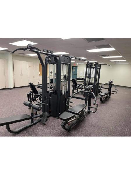Black 8-stack multi-gym with various exercise stations in a well-lit room with white cabinets.