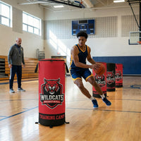 Thumbnail for Basketball player dribbling around red custom pop-up defenders with a "Wildcats" logo on a gym court.
