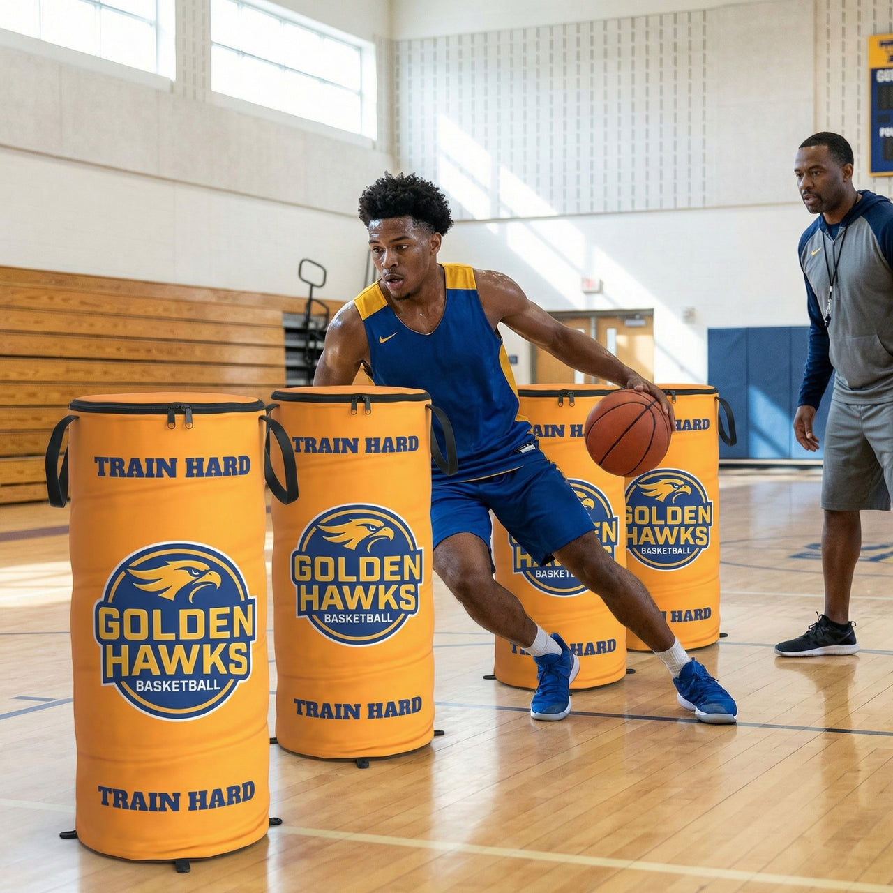 Basketball player dribbling around three orange custom pop-up defenders with "Golden Hawks Basketball" logo.