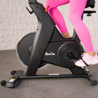 Thumbnail for Person in pink leggings and sneakers pedaling a black BanCon upright exercise bike.