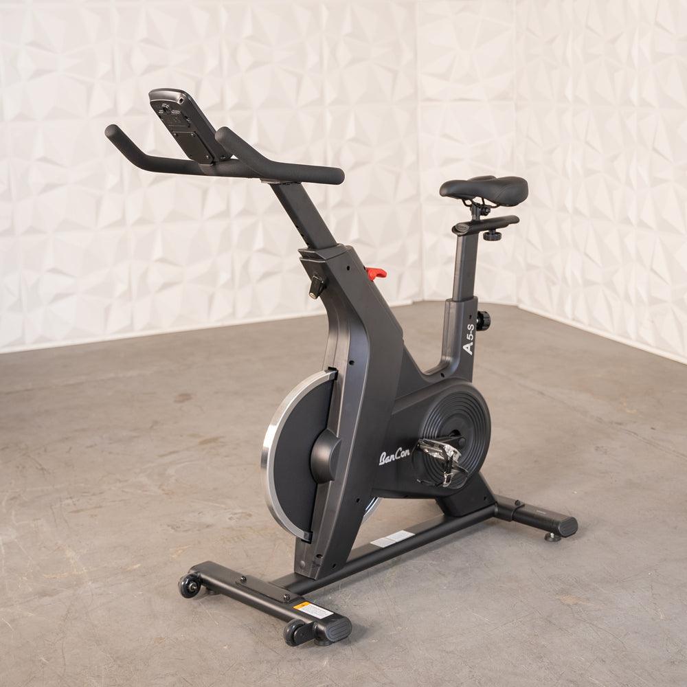 Black upright exercise bike with adjustable seat and handlebars on a concrete floor.
