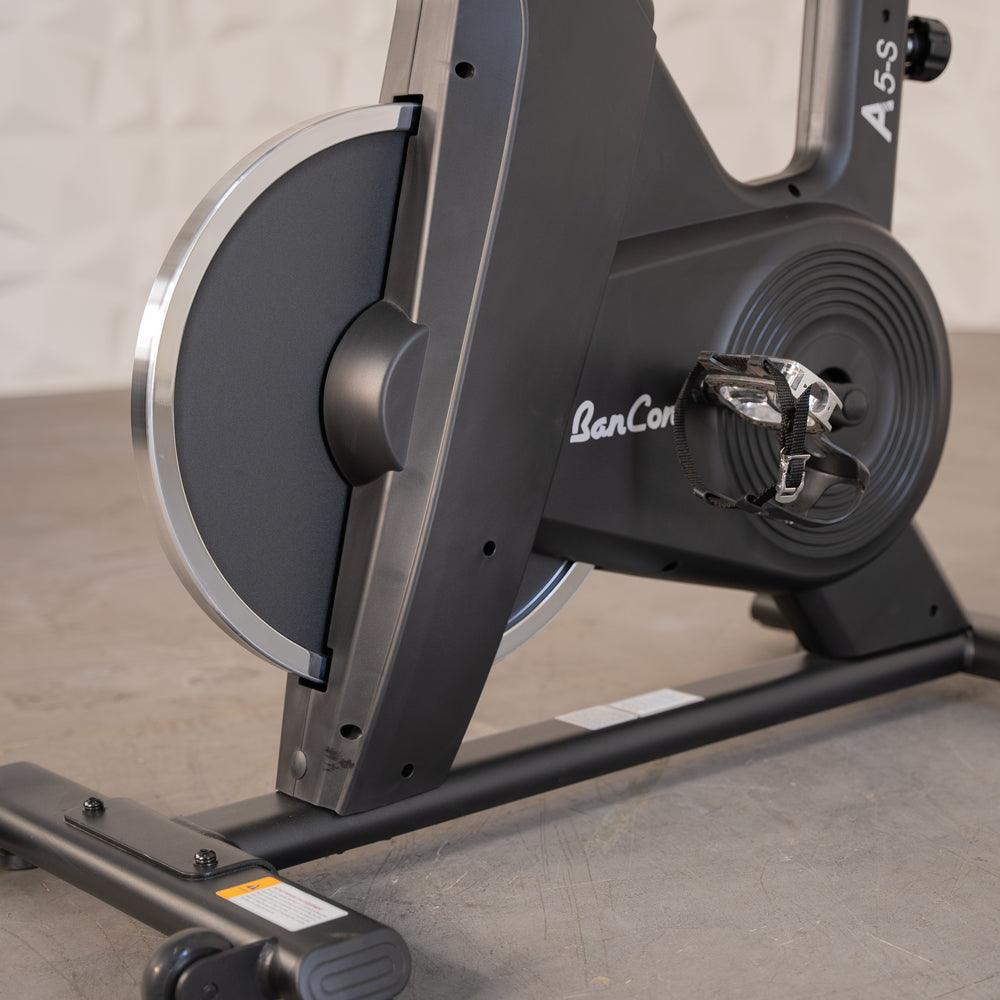Close-up of a black exercise bike's flywheel, pedal, and base.