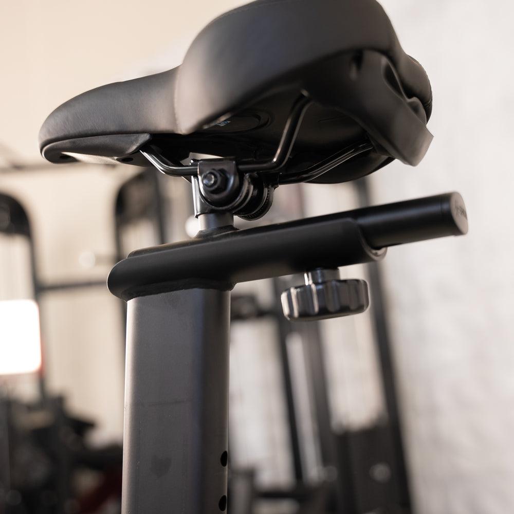 Close-up of an exercise bike's black seat and adjustable post with a knob.