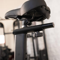 Thumbnail for Close-up of an exercise bike's black seat and adjustable post with a knob.