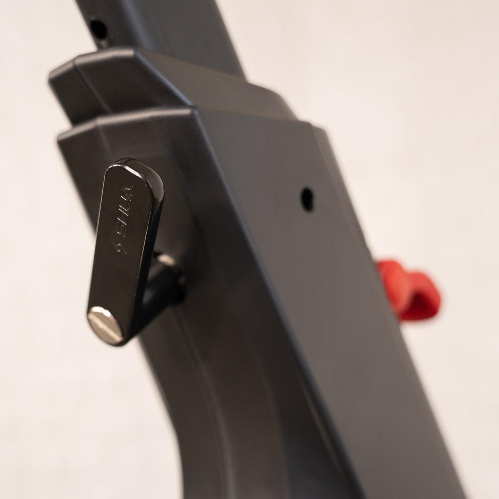 Close-up of the black adjustment lever on an exercise bike, with a red knob visible in the background.