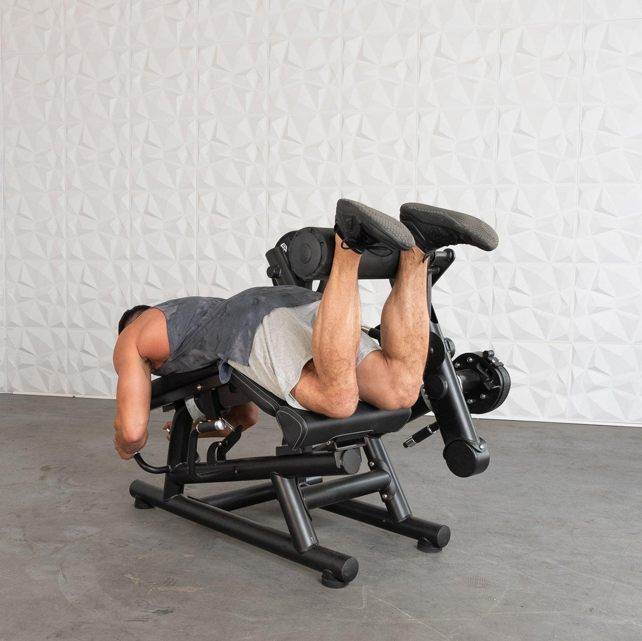Man performing leg curls on a black plate-loaded fitness machine.