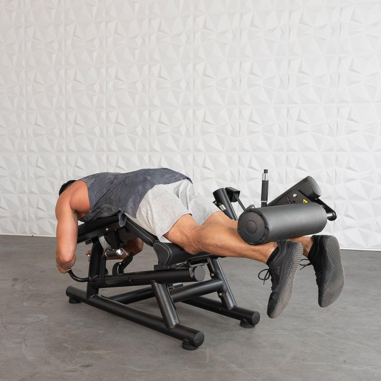 Man using a black leg extension/curl machine, lying prone with his legs extended.