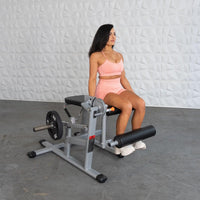 Thumbnail for Woman in peach activewear sitting on a silver and black leg extension/curl machine with a weight plate.