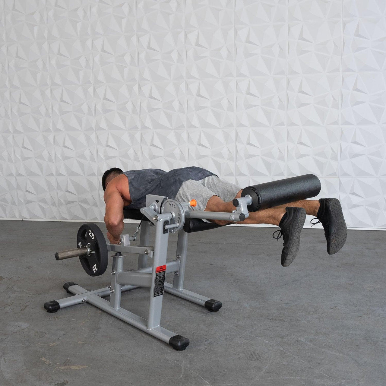 Man performing leg curls on a silver and black plate-loaded fitness machine.