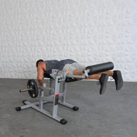 Thumbnail for Man performing leg curls on a silver and black plate-loaded fitness machine.