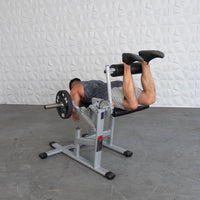 Thumbnail for Man performing leg curls on a silver and black plate-loaded fitness machine.