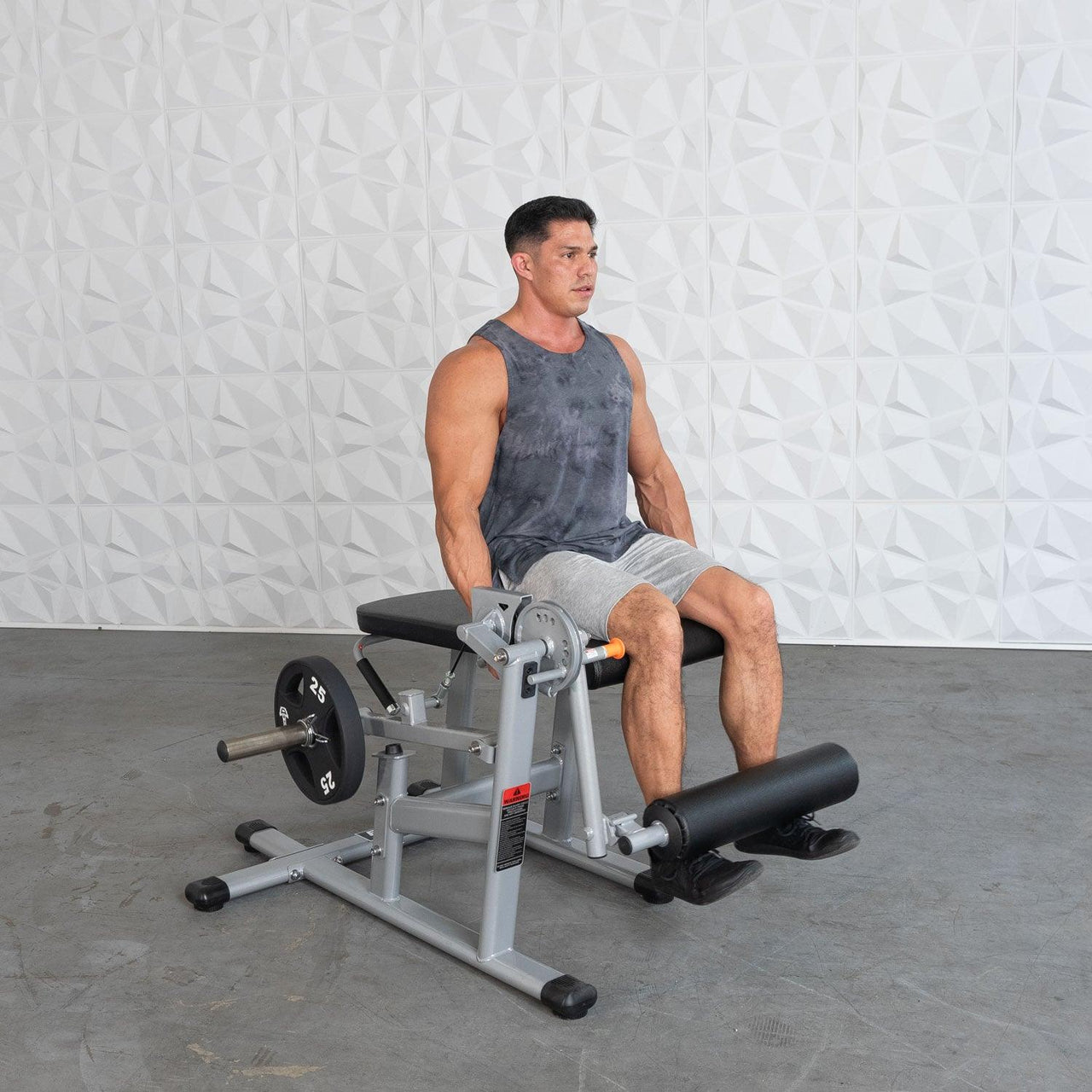 Man using a silver and black plate-loaded leg extension/leg curl machine with a 25lb weight plate.